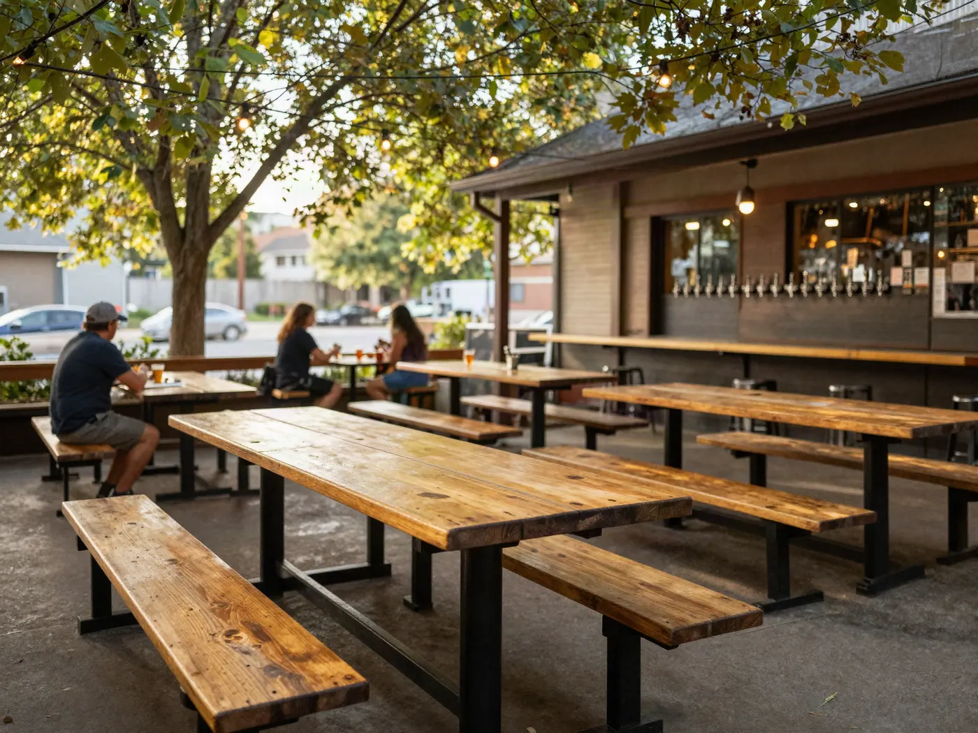 El patio a la tarde, con mesas largas de madera bajo los árboles.